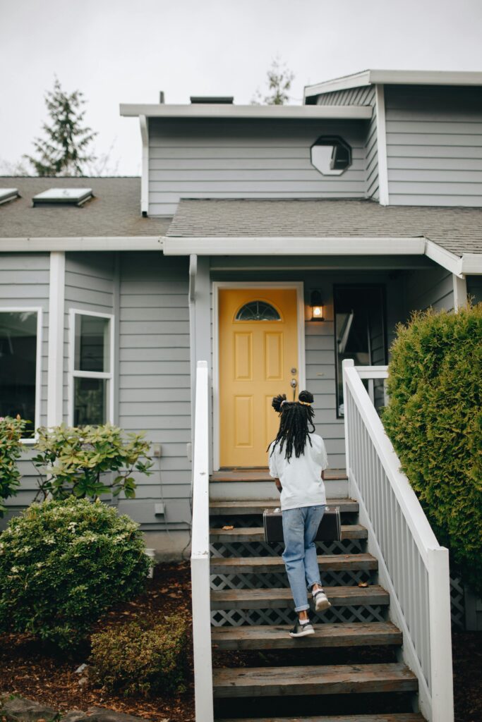 pexels-photo-7577377-7577377 Back view of a girl walking up wooden stairs towards a house with a yellow door.